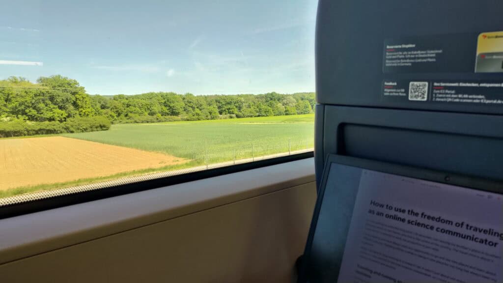 Laptop on a train with an article open, titled "Using the freedom of traveling as an online science communicator productively".
