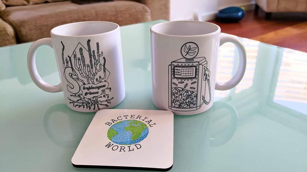Cups and coaster with illustrations from the bacterial colouring book and showing the logo of BacterialWorld
